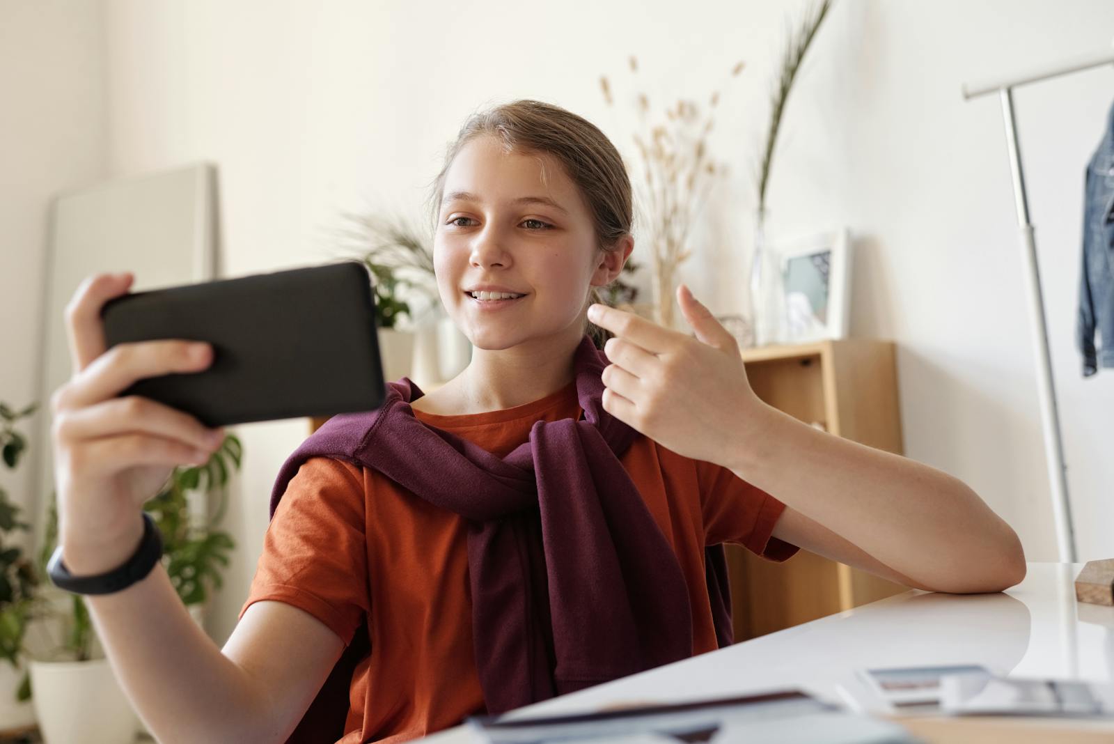 Smiling teenage girl making a video call at home using a smartphone, emphasizing connection and communication.